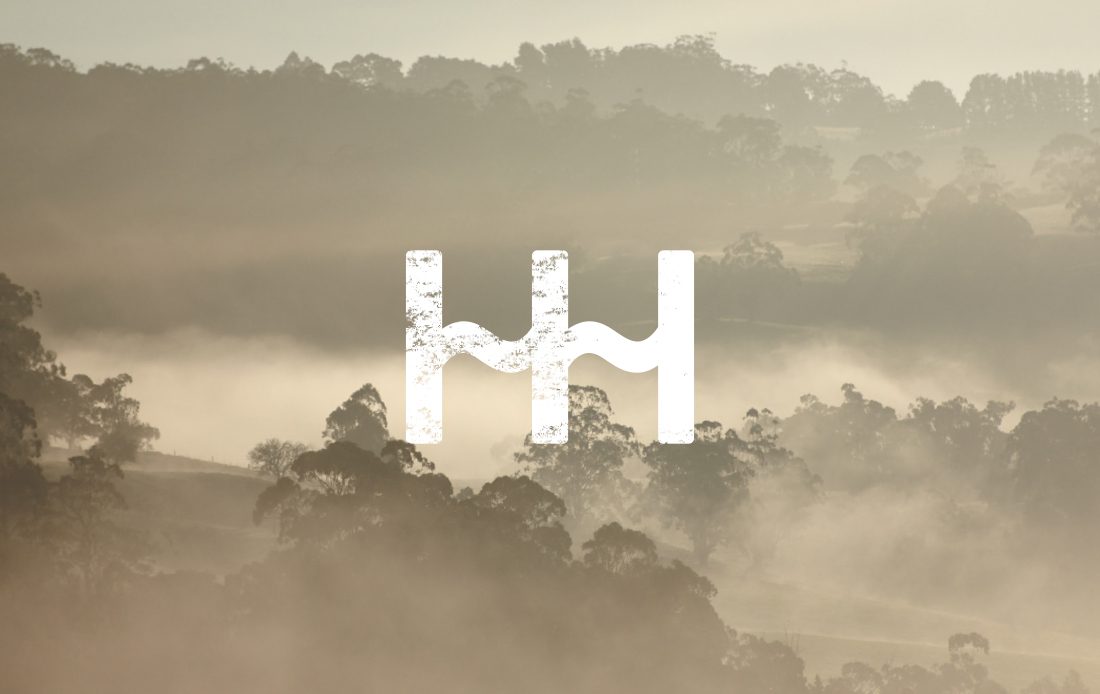 Hidden Hill logo layered landscape of trees and mist during in sunrise