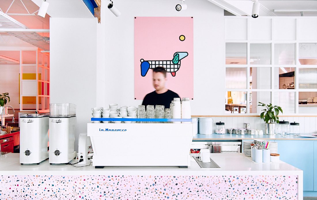 Barista at coffee machine with pink dog poster in background